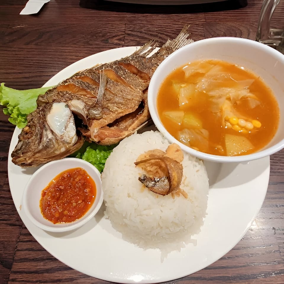 Indonesian fried fish with rice, spicy sambal, and a vegetable soup on a white plate.