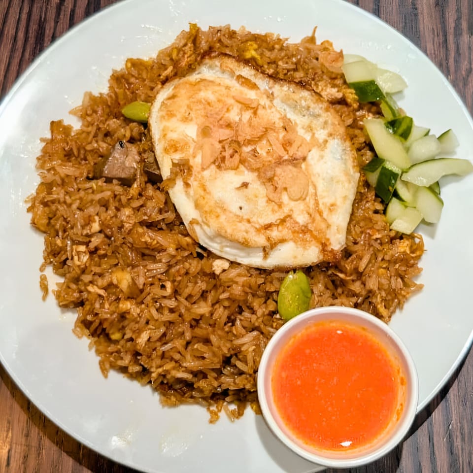 Indonesian Nasi Goreng with a fried egg, cucumber slices, and a side of chili sauce.