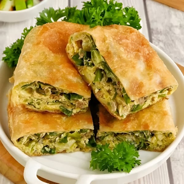 Four pieces of golden-brown Indonesian Martabak, filled with egg and green vegetables, garnished with parsley.