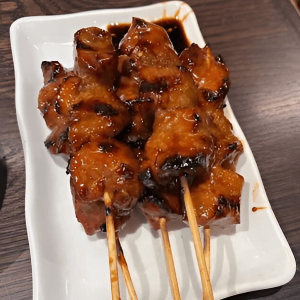 Indonesian chicken satay skewers with a glossy brown sauce on a white rectangular plate.