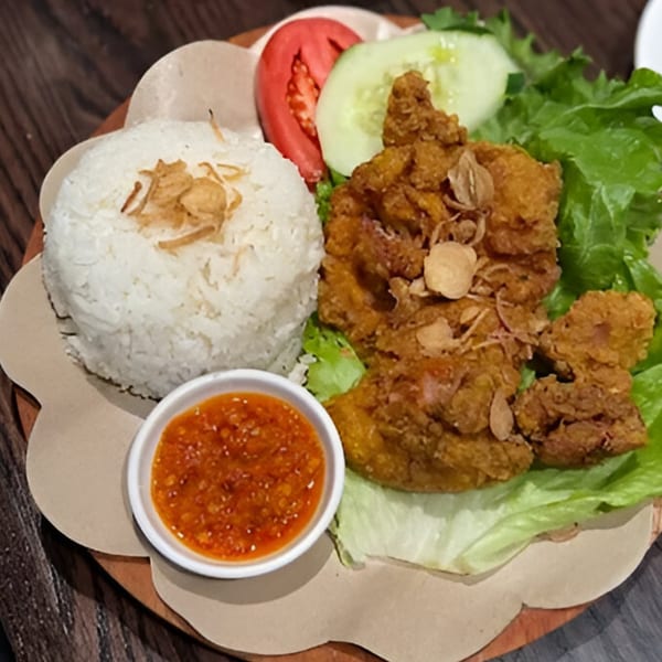 Indonesian fried chicken with rice, chili sauce, lettuce, tomato, and cucumber on a wooden plate.