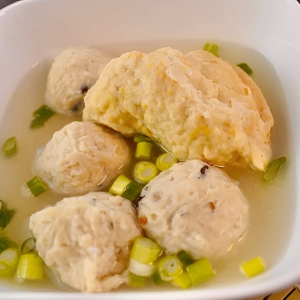 Indonesian chicken meatballs in clear broth, garnished with chopped green onions, served in a white bowl.