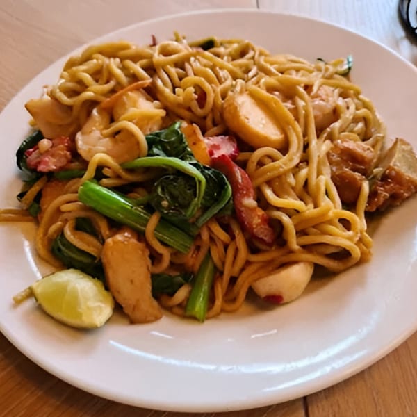 Indonesian stir-fried noodles with shrimp, vegetables, and a lime wedge on a white plate.