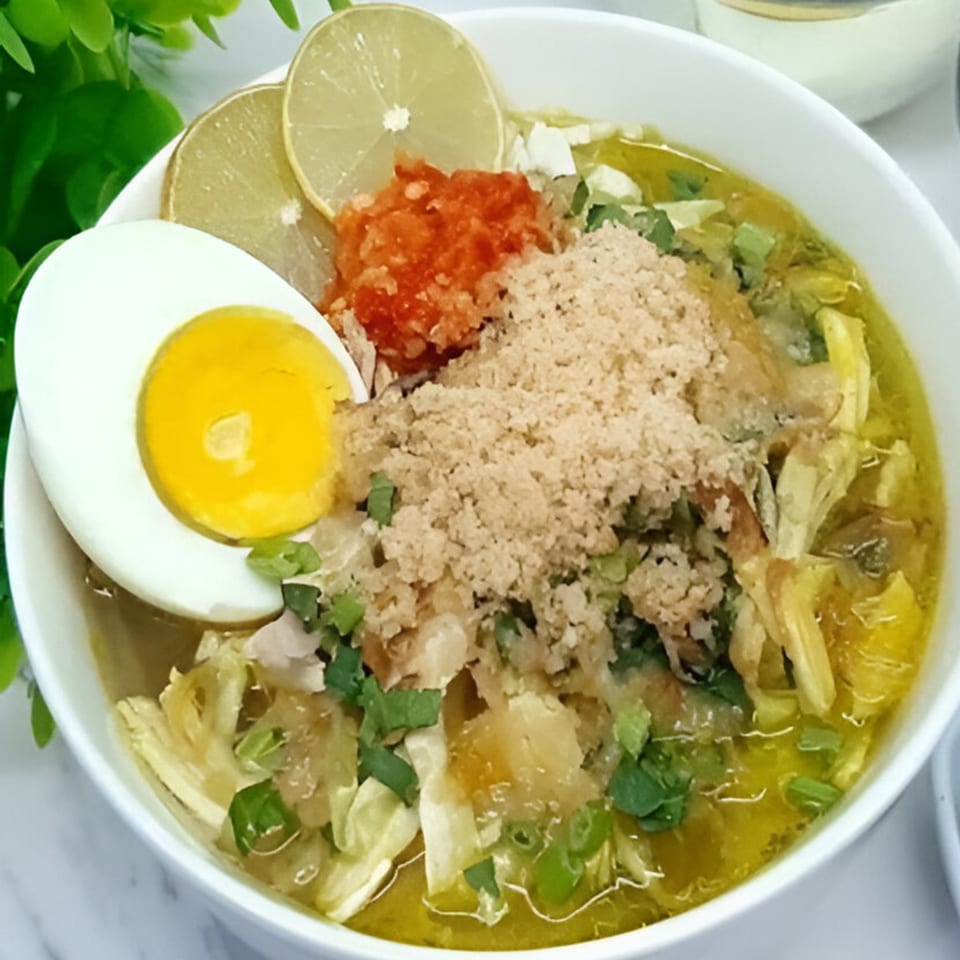 Close-up of Indonesian Soto Ayam, a chicken soup with egg, lime, chili, and fried shallots.
